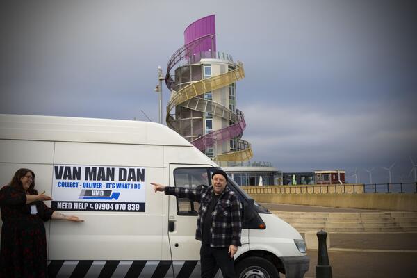 Woman and Man standing either side of a white van with a logo saying 'Van Man Dan. Seaside in the background..